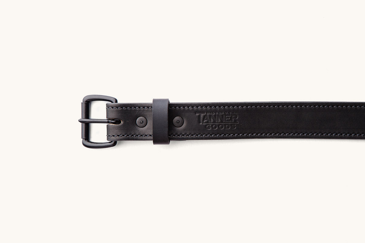 a black belt with black buckle and tanner goods monogram