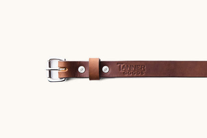 the first half of a brown leather belt with silver hardware and a Tanner Goods logo monogram